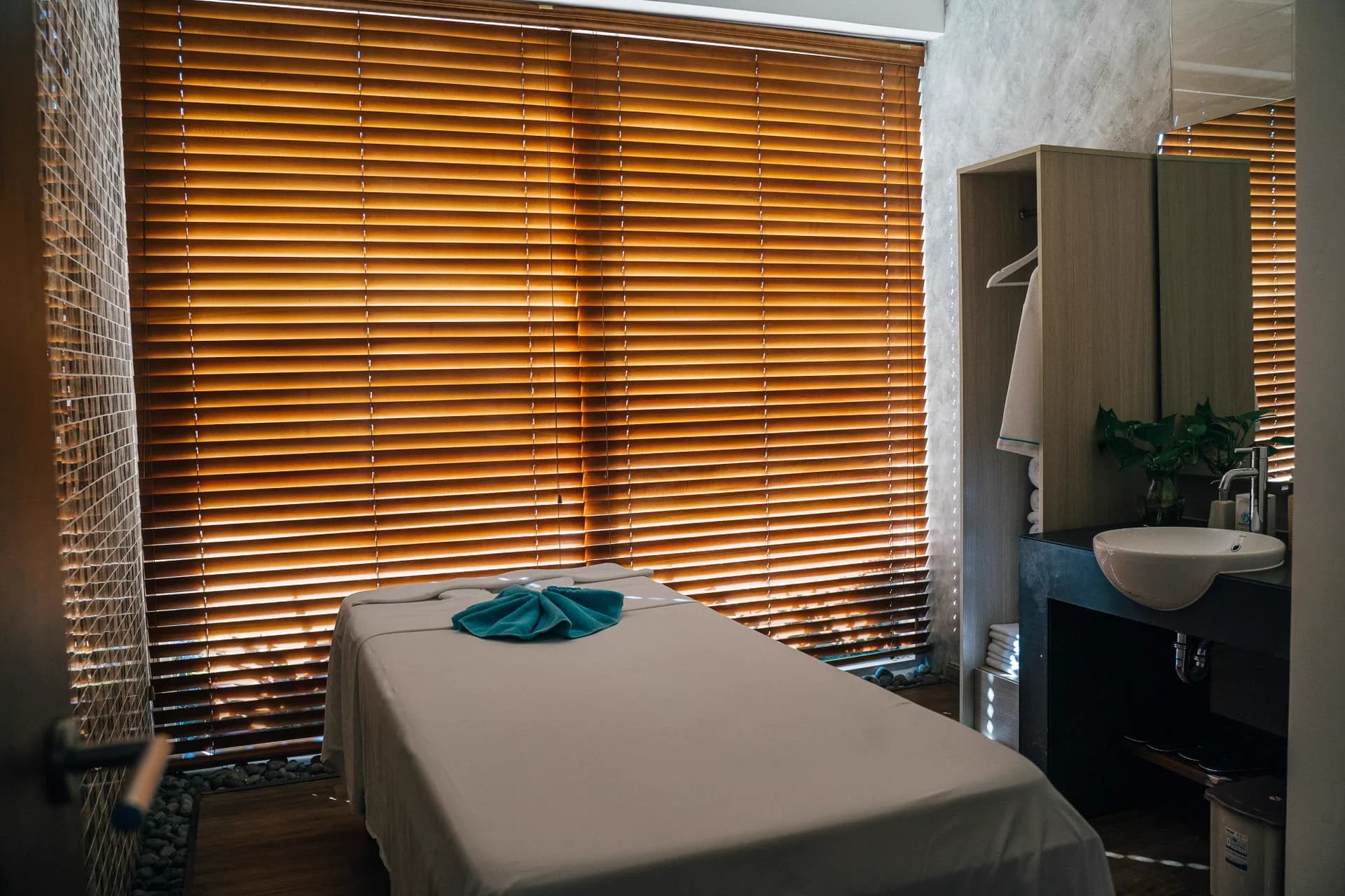 Table de massage préparée devant de larges stores de bois qui filtrent la lumière