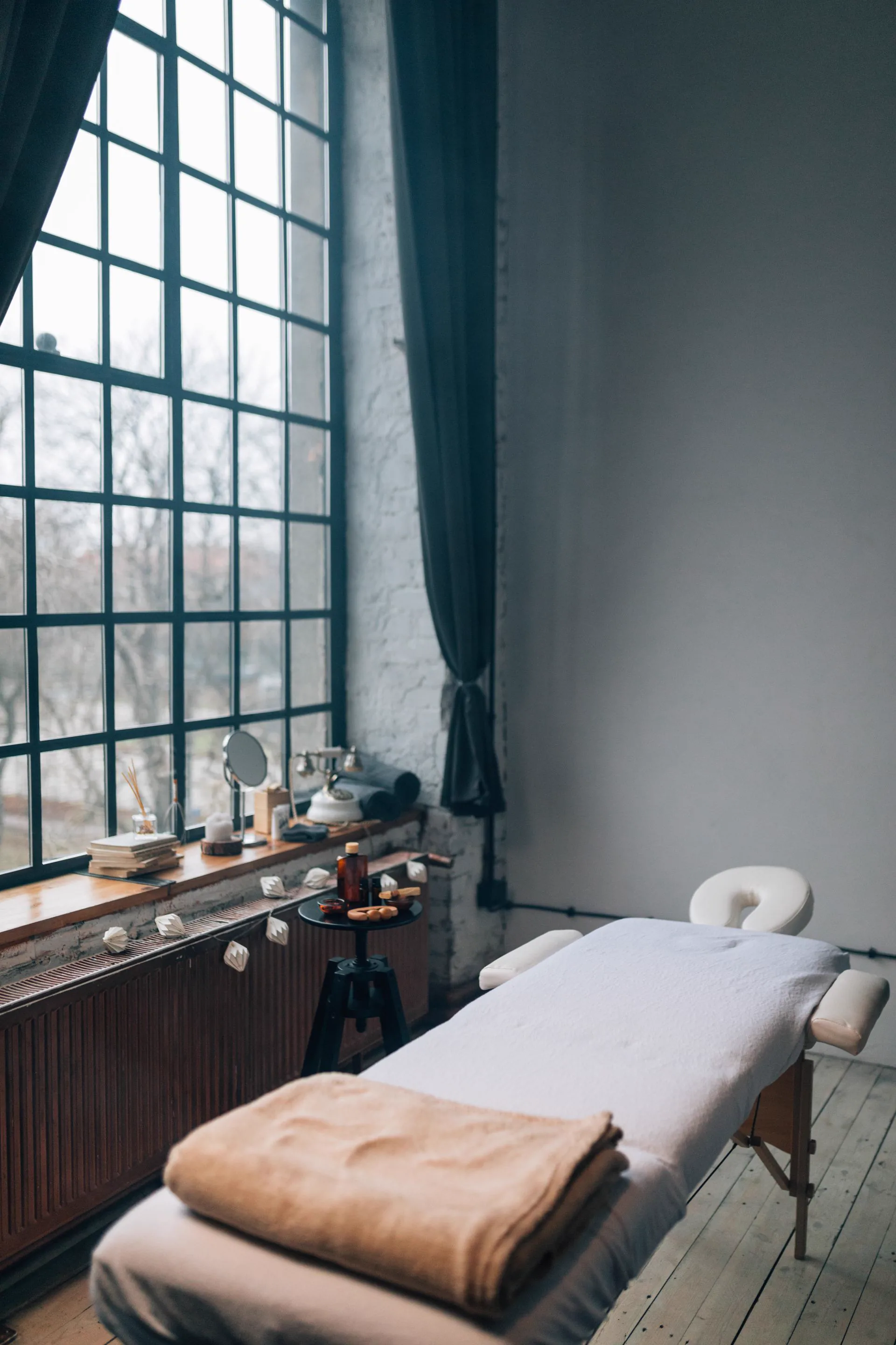 A massage couch set up in front of a tall window, a folded blanket in the foreground