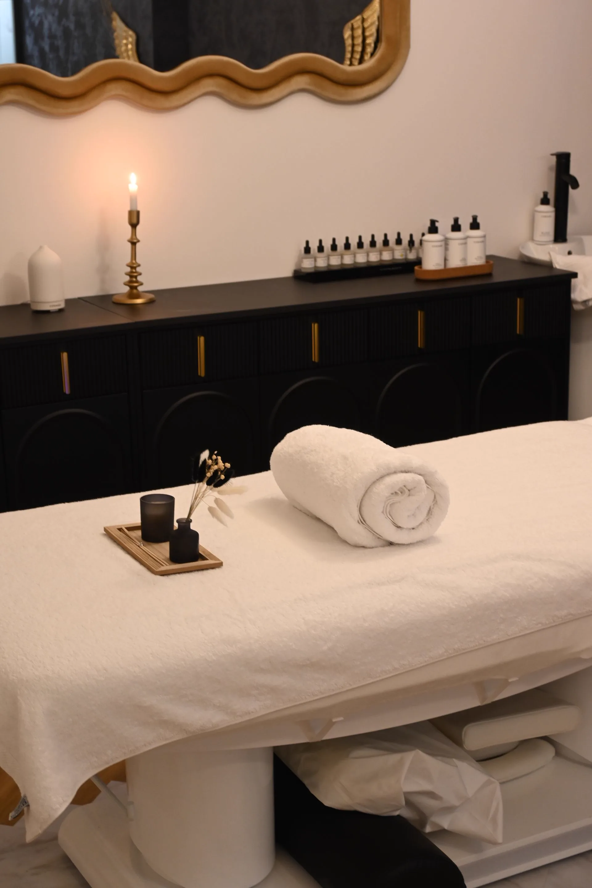 A couch dressed in white with a rolled towel, a candle lit on the sideboard behind