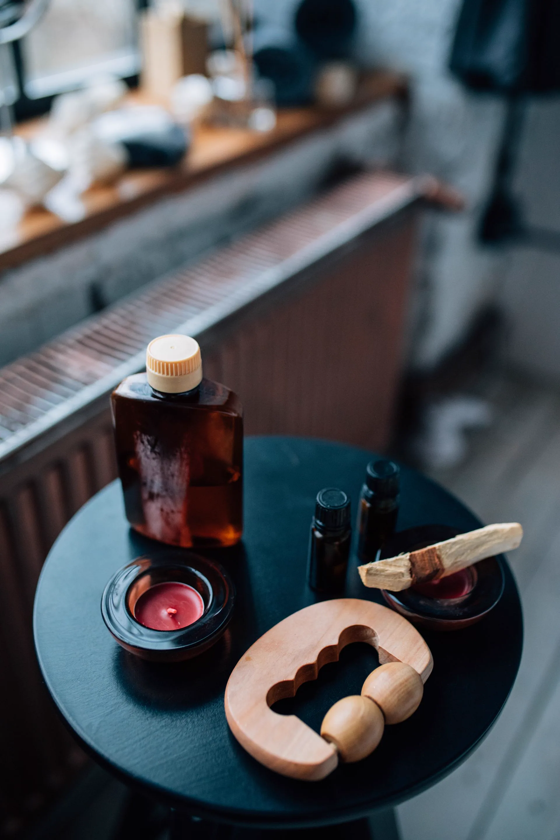 A wooden maderotherapy tool on a round side table, beside a bottle of oil and two candles